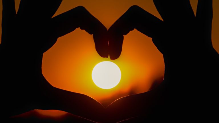 Zwei Hände formen ein Herz vor der untergehenden Sonne